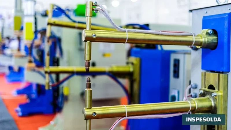 Braços e eletrodos de cobre de uma máquina de solda a ponto, com outras máquinas iguais ao fundo