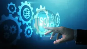 Mão toca ícone com a sigla ISO cercado por engrenagens em fundo azul digital.