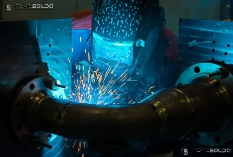 Soldador em tubulação curva com flanges, sob luz azul e com faíscas