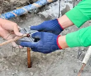 Mãos com luvas seguram um molde de solda exotérmica sobre cabos no chão.