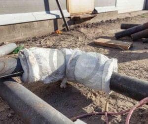 Trecho de tubulação enrolado em manta térmica, apoiado no chão de uma obra.