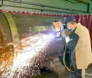 Técnicos operando máquina de solda por resistência em ambiente fabril.